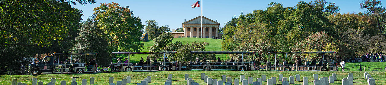 Arlington Tours vehicle driving past Arlington House in background and grave sites and trees in foreground