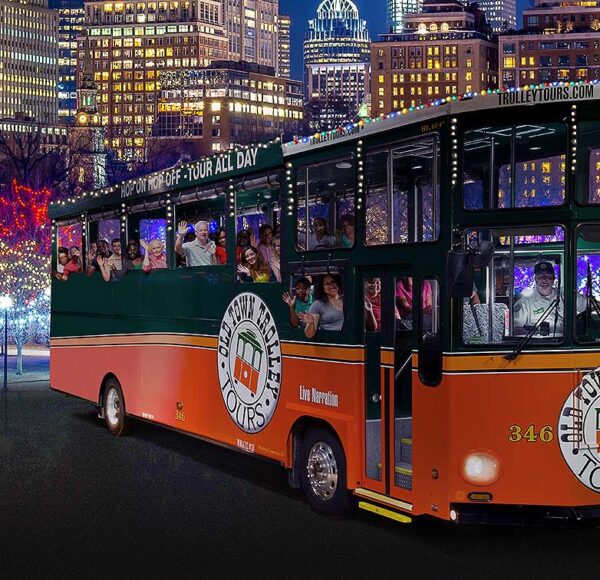 night time picture of trolley in front of Boston skyline and holiday lights