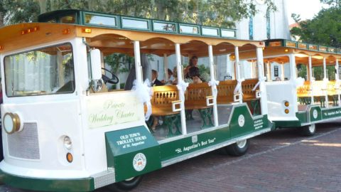 A modified wedding Old Town Trolley painted in white and green parked outside a church in St. Augustine, FL